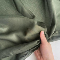 Une main tient et rassemble délicatement le Soie de coton multicolore au mètre de Longan Craft France, un tissu de doublure en soie de mûrier léger et respirant, mettant en valeur sa texture diaphane et aérienne sur un fond neutre.