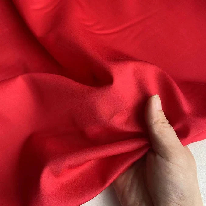 Une main tient et regroupe la Soie de coton multicolore au mètre de Longan Craft France, mettant en valeur la texture lisse et l'éclat de la soie de mûrier légère sous la lumière - idéale comme tissu de doublure respirant.
