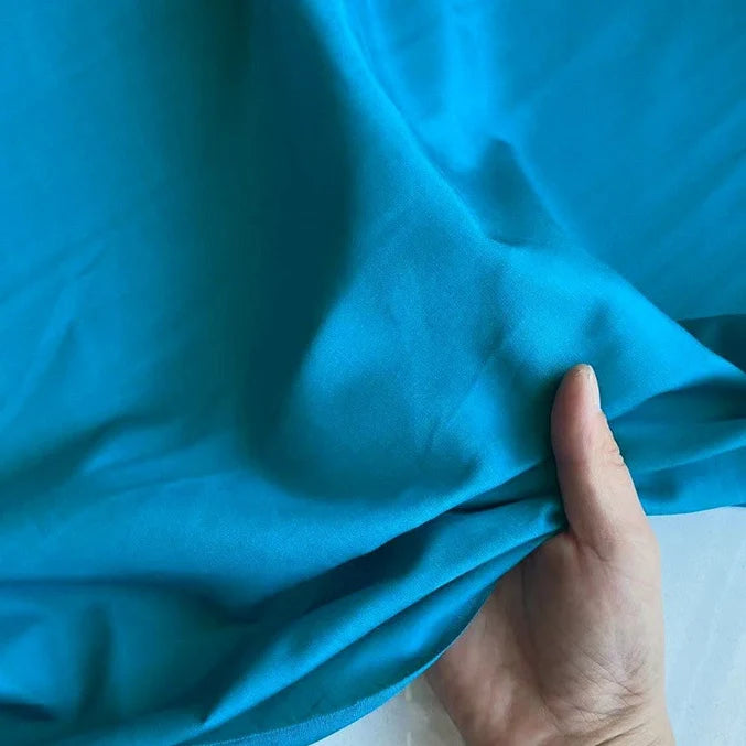Une main soulève une Soie de coton multicolore au mètre de Longan Craft France-une Soie de mûrier légère, idéale comme tissu de doublure en soie respirant.