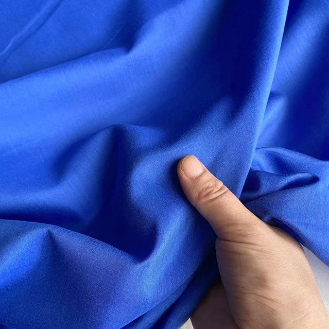 Une main tient et froisse Soie de coton multicolore au mètre de Longan Craft France, un tissu de doublure en soie de mûrier léger et respirant, mettant en valeur sa texture lisse et sa flexibilité.
