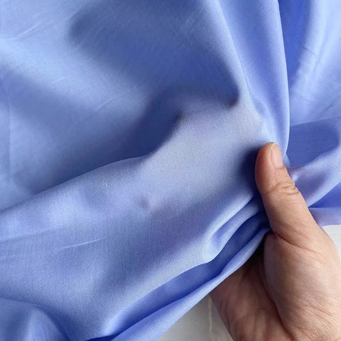 Une main tient et froisse légèrement un tissu léger Soie de coton multicolore au mètre de Longan Craft France, mettant en valeur la texture lisse et respirante de cette soie de mûrier doublure avec de légers plis et froissures.
