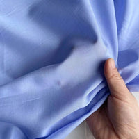 Une main tient et froisse légèrement un tissu léger Soie de coton multicolore au mètre de Longan Craft France, mettant en valeur la texture lisse et respirante de cette soie de mûrier doublure avec de légers plis et froissures.