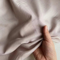 Une main rassemble un morceau de Soie de coton multicolore au mètre de Longan Craft France, un mélange léger de soie et de coton de couleur mûre à la texture lisse et au lustre subtil, parfait comme tissu de doublure en soie respirante.