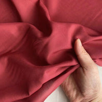 Une main tient et rassemble délicatement un morceau de Longan Craft France Soie de coton multicolore au mètre, un tissu de doublure en soie de mûrier léger et respirant, mettant en valeur sa texture lisse et son drapé élégant sur un fond neutre.