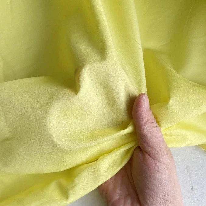 Une main tient un morceau de Soie de coton multicolore au mètre de Longan Craft France, mettant en valeur la texture luxueuse et légère de ce tissu de doublure en soie de mûrier respirant.