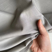 Une main tient un morceau de Soie de coton multicolore au mètre de Longan Craft France et l'enroule délicatement, mettant en valeur la texture légère et respirante de cette soie de mûrier légère doublure en soie.