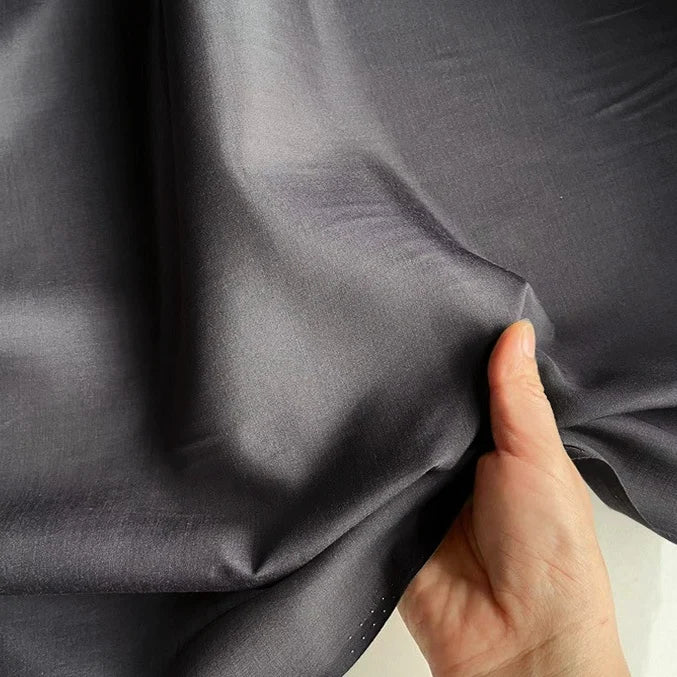 Une main pince un morceau de Longan Craft France Soie de coton multicolore au mètre, montrant la texture lisse et la brillance de cette légère soie de mûrier, un tissu de doublure en soie respirant.