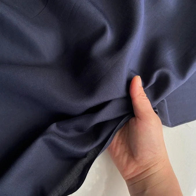 Une main tient un morceau de Soie de coton multicolore au mètre de Longan Craft France, mettant en valeur la texture légère et souple de ce tissu de doublure en soie de mûrier respirant sur un fond neutre.