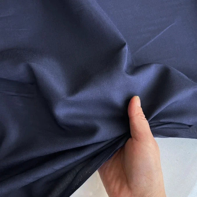 Une main tient et rassemble un morceau de Soie de coton multicolore au mètre | Soie de mûrier légère | Tissu de doublure en soie respirant de Longan Craft France, montrant sa texture douce et sa brillance subtile sur un fond clair.