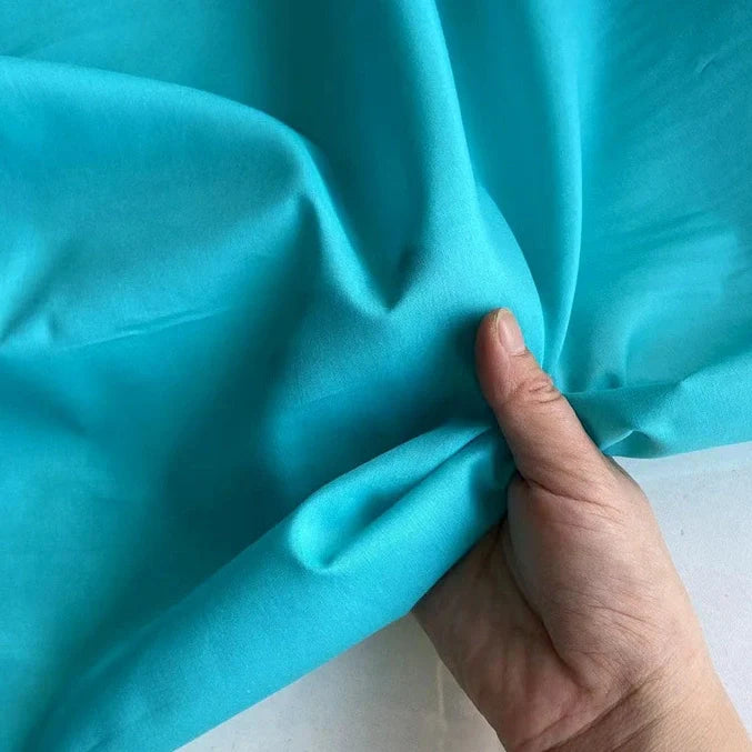 Une main tient et froisse délicatement Soie de coton multicolore au mètre de Longan Craft France, un tissu de doublure en soie (soie de mûrier) léger et respirant, mettant en valeur sa texture lisse et sa souplesse.