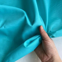 Une main tient et froisse délicatement Soie de coton multicolore au mètre de Longan Craft France, un tissu de doublure en soie (soie de mûrier) léger et respirant, mettant en valeur sa texture lisse et sa souplesse.