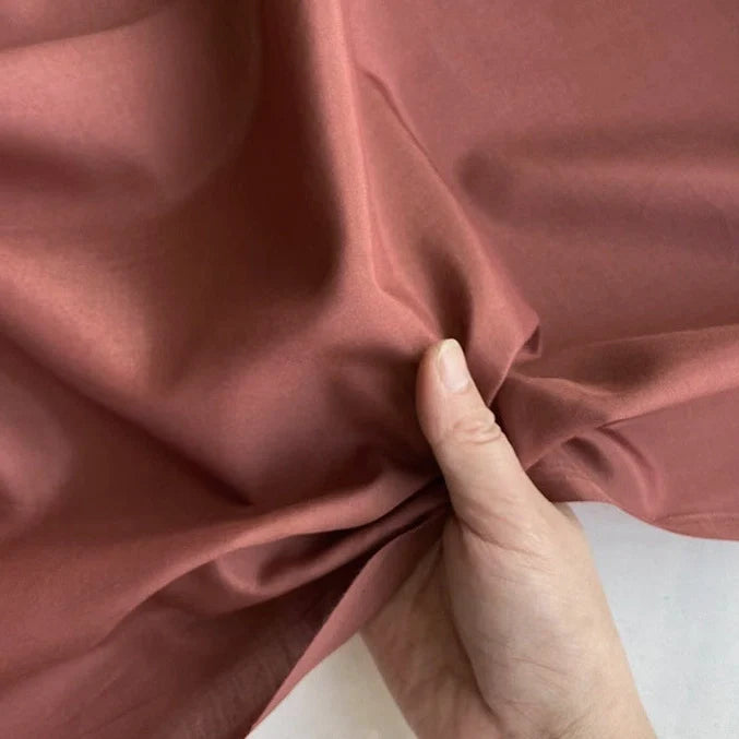 Une main tenant et rassemblant délicatement un morceau de Soie de coton multicolore au mètre de Longan Craft France, révélant la texture légère et lisse ainsi que la qualité respirante de ce tissu de soie de mûrier doublure.