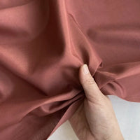 Une main tenant et rassemblant délicatement un morceau de Soie de coton multicolore au mètre de Longan Craft France, révélant la texture légère et lisse ainsi que la qualité respirante de ce tissu de soie de mûrier doublure.