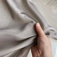 Une main tient un morceau de Soie de coton multicolore au mètre de Longan Craft France, révélant la texture douce et respirante ainsi que la surface lisse et luxueuse de ce léger tissu de doublure en soie de mûrier.