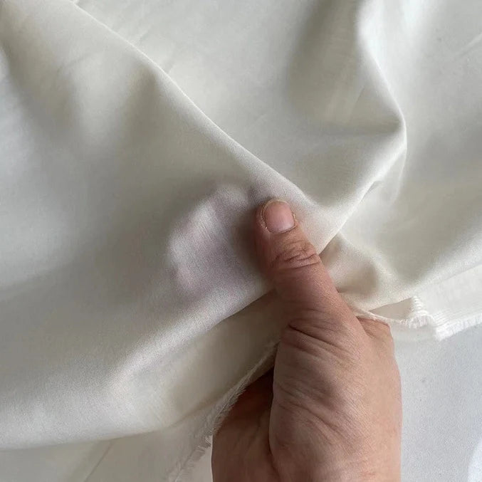 Une main tient un morceau de Soie de coton multicolore au mètre semi-transparent de Longan Craft France, montrant sa souplesse et son bord délicat et légèrement irrégulier. Idéale comme doublure en soie légère et respirante.