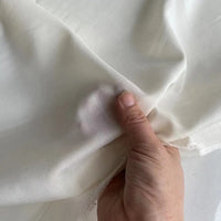 Une main tient un morceau de Soie de coton multicolore au mètre semi-transparent de Longan Craft France, montrant sa souplesse et son bord délicat et légèrement irrégulier. Idéale comme doublure en soie légère et respirante.