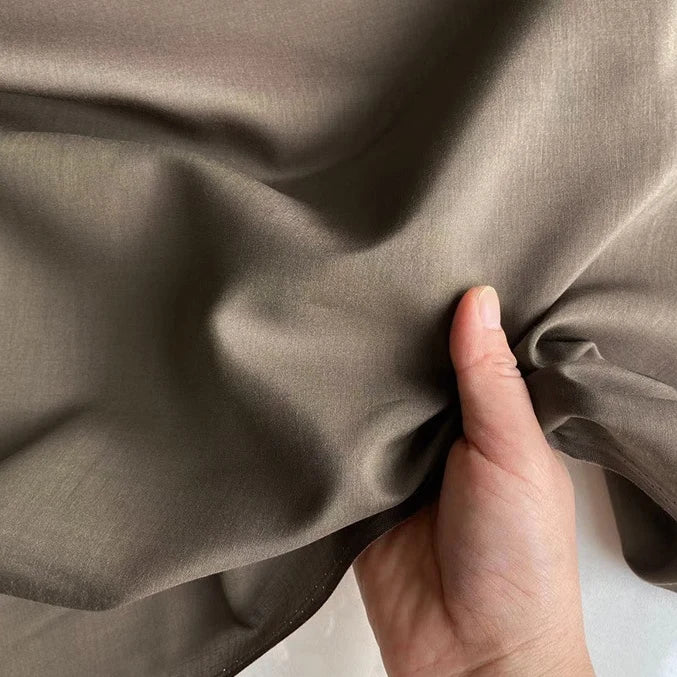 Une main tient Soie de coton multicolore au mètre de Longan Craft France, un tissu de doublure en soie mûrier respirant et léger, mettant en valeur sa texture douce et son drapé gracieux.