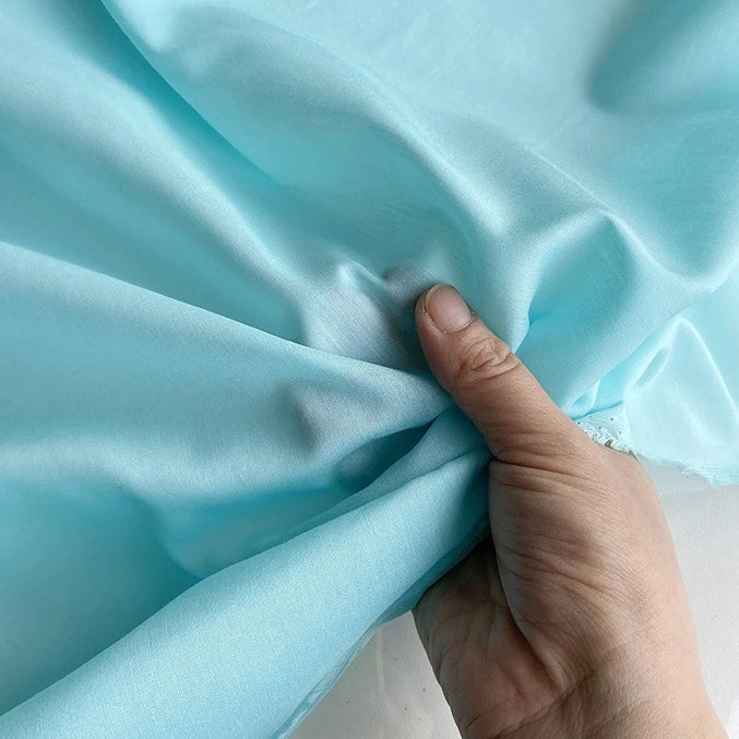 Une main tire délicatement sur un morceau de Soie de coton multicolore au mètre de Longan Craft France, révélant la texture douce et légère et la brillance de ce tissu de doublure en soie de mûrier léger et perméable à l'air.