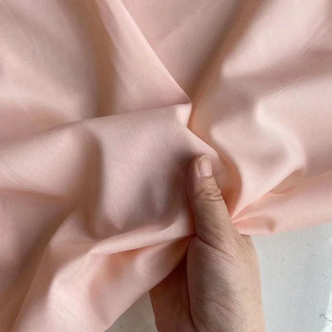 Une main tient et fronce Soie de coton multicolore au mètre de Longan Craft France, un tissu de doublure en soie de mûrier clair, mettant en valeur sa texture lisse et respirante et ses plis doux.