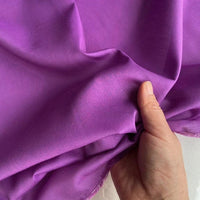 Une main soulève un morceau de Soie de coton multicolore au mètre, lisse et brillant, de Longan Craft France, mettant en valeur la texture et le drapé délicats de ce tissu de doublure en soie de mûrier, léger et respirant.