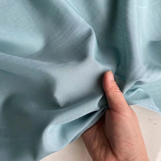 Une main tient et fronce Soie de coton multicolore au mètre de Longan Craft France, un tissu léger de doublure en soie de murier, mettant en valeur sa texture lisse et sa brillance douce.