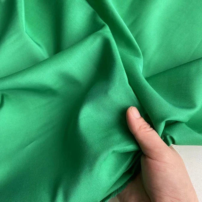 Une main tient un morceau de Soie de coton multicolore au mètre de Longan Craft France, un tissu de soie de mûrier doublure, léger et respirant, d'un vert vif, qui présente une texture douce avec de légers plis.