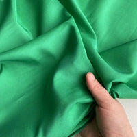 Une main tient un morceau de Soie de coton multicolore au mètre de Longan Craft France, un tissu de soie de mûrier doublure, léger et respirant, d'un vert vif, qui présente une texture douce avec de légers plis.