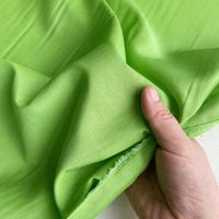 Une main tient un morceau de Soie de coton multicolore au mètre de Longan Craft France, mettant en valeur sa texture lisse, sa couleur vert vif et son bord non fini - un tissu de doublure en soie léger et respirant.