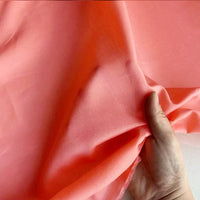 Une main soulève une Soie de coton au mètre multicolore, légère et transparente, de Longan Craft France, fabriquée à partir de soie de mûrier respirante, à la texture lisse et translucide, idéale pour les doublures.