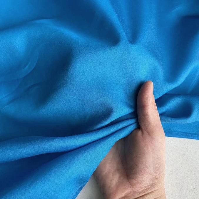 Une main fronce un morceau léger de Soie de coton multicolore au mètre de Longan Craft France, mettant en valeur la texture douce et la brillance subtile de ce tissu respirant de doublure en soie de mûrier.