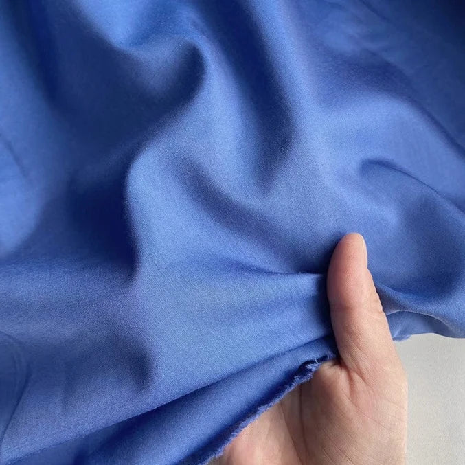 Une main soulève un morceau de Soie de coton multicolore au mètre de Longan Craft France - une soie de mûrier doublure légère et respirante - révélant la texture lisse et les plis subtils de ce tissu de soie de première qualité.