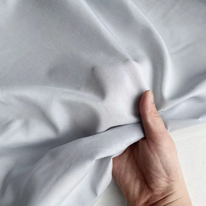 Une main tient délicatement la vibrante Soie de coton multicolore de Longan Craft France, mettant en valeur le tissu doux et léger en soie de mûrier, parfait pour une doublure respirante.