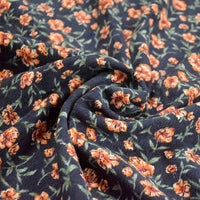 Gros plan sur le tissu velours côtelé à fleurs colorées au mètre de Longan Craft France, un tissu bleu foncé orné de petites fleurs orange et de feuilles vertes, froncé au centre pour souligner sa qualité texturée et épaisse.