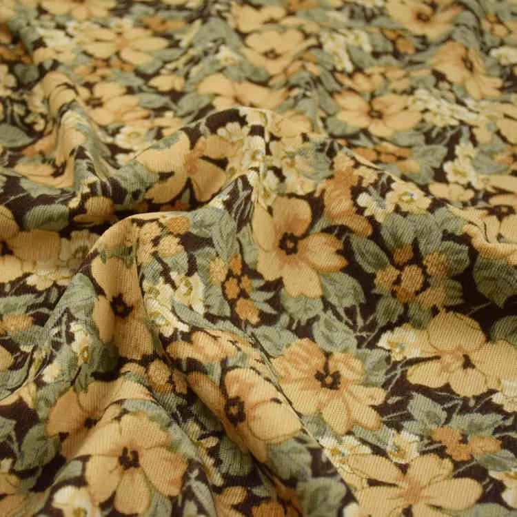 Un gros plan de Tissu velours côtelé à fleurs colorées au mètre de Longan Craft France montre sa texture avec motifs floraux jaunes et beiges, feuilles vertes et fond foncé, idéal pour confection, ameublement et loisirs créatifs.