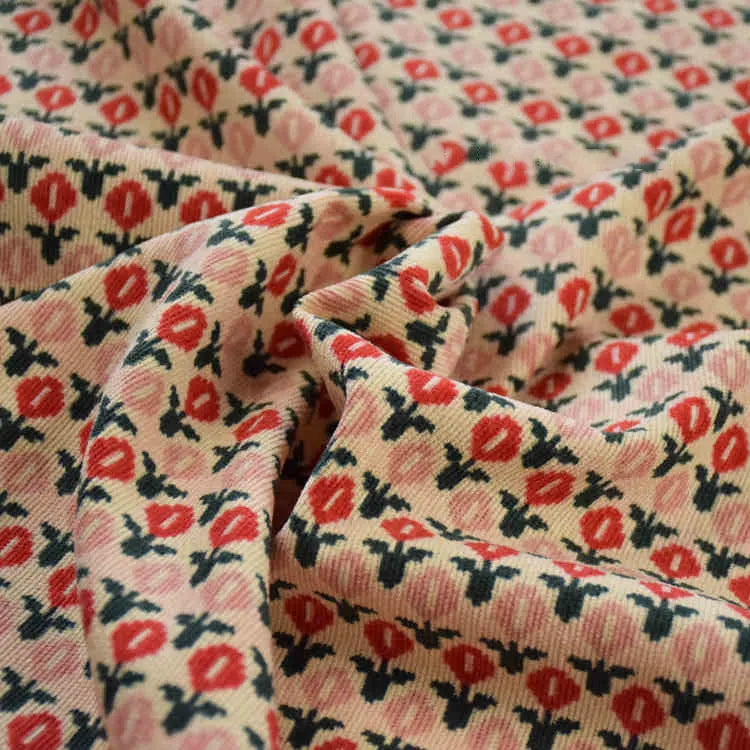Gros plan sur le tissu velours côtelé à fleurs colorées de Longan Craft France, montrant de petites fleurs rouges et roses avec des feuilles vertes sur un fond beige clair - parfait pour la couture, la décoration et l'artisanat.