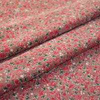 Un gros plan du tissu velours côtelé à fleurs colorées de Longan Craft France montre des fleurs rouges, des feuilles vertes et des accents blancs sur un rose discret, avec une texture tissée visible - parfait pour la couture, la décoration et l'artisanat au mètre.