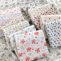 Des carrés pliés de Tissu plumetis blanc imprimé de fleurs de Longan Craft France, un tissu de plumetis de coton à motifs floraux, sont présentés sur une surface de tissu floral assorti.
