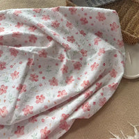 Un morceau de Tissu plumetis blanc imprimé de fleurs de Longan Craft France est présenté sur une surface beige à côté d'un panier en osier et d'un plateau blanc.