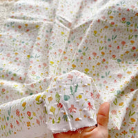 Une main tient Tissu plumetis blanc imprimé de fleurs au mètre de Longan Craft France, un plumetis de coton doux avec un motif floral - idéal pour créer des vêtements d'intérieur ou utiliser comme tissu coton au mètre pour votre prochain projet de couture.