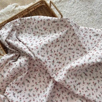 Un panier en osier est partiellement recouvert par le tissu plumetis blanc imprimé de fleurs de Longan Craft France, un tissu de coton avec un motif floral, reposant sur une surface légèrement texturée.