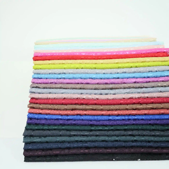 Une pile de tissu damassé jacquard multicolore de Longan Craft France, avec des motifs floraux, est soigneusement pliée en couches sur un fond blanc.