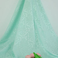 Gros plan sur le tissu jacquard damassé multicolore au mètre de Longan Craft France, un textile d'ameublement à motif floral, drapé en plis, avec deux roses artificielles roses et des feuilles vertes soulignant son design élégant.