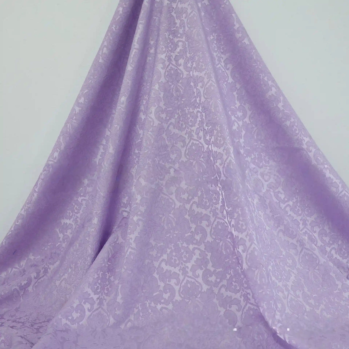 Une longueur de tissu damassé jacquard multicolore de Longan Craft France, présentant un subtil motif floral, se détache sur un fond blanc. Le textile d'ameublement capte la lumière et se drape en douceur jusqu'au sol.