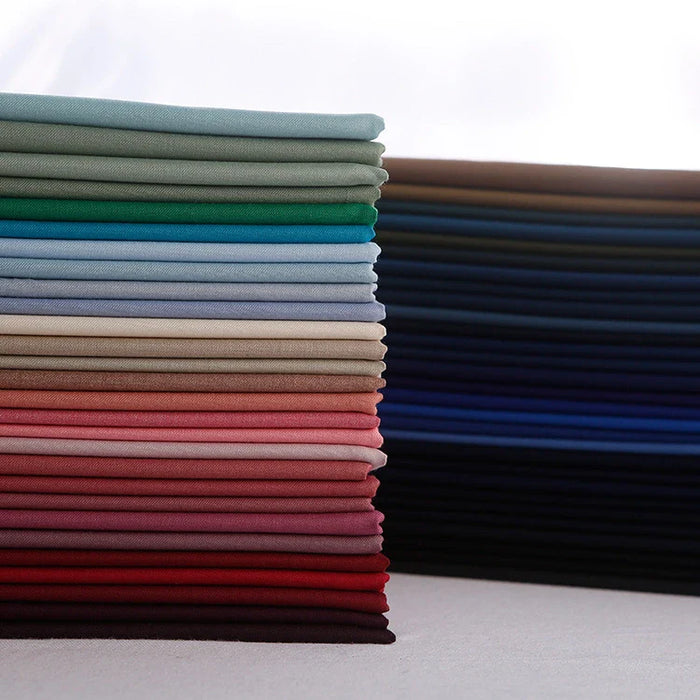 Une pile colorée de rayonne polyester Tissu gabardine pliée de Longan Craft France, parfaite pour les uniformes de bricolage, est disposée sur une surface plane dans des tons verts, bleus, blancs, roses, rouges et sombres sur un fond lumineux.