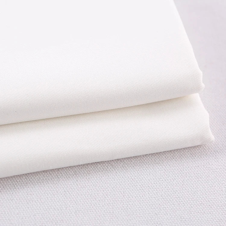 Deux pièces de gabardine polyester rayonne de Longan Craft France, soigneusement pliées, sont empilées sur une surface claire. Ce textile épais, idéal pour le bricolage d'uniformes et de robes, présente une texture lisse et subtilement visible et est vendu au mètre.