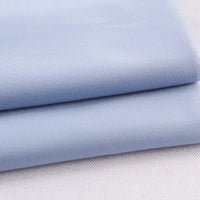 Deux pièces soigneusement pliées du tissu gabardine polyester rayonne coloré au mètre de Longan Craft France, une gabardine épaisse et lisse parfaite pour les uniformes de bricolage, sont empilées sur une surface claire, montrant sa douce finition mate.