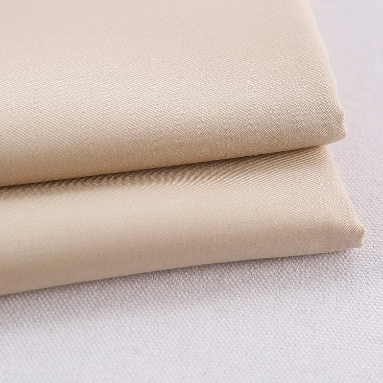 Deux pièces de tissu Longan Craft France gabardine polyester rayonne coloré au mètre sont soigneusement pliées et empilées sur une surface blanc cassé - un textile gabardine épais parfait pour les uniformes et les projets de bricolage.