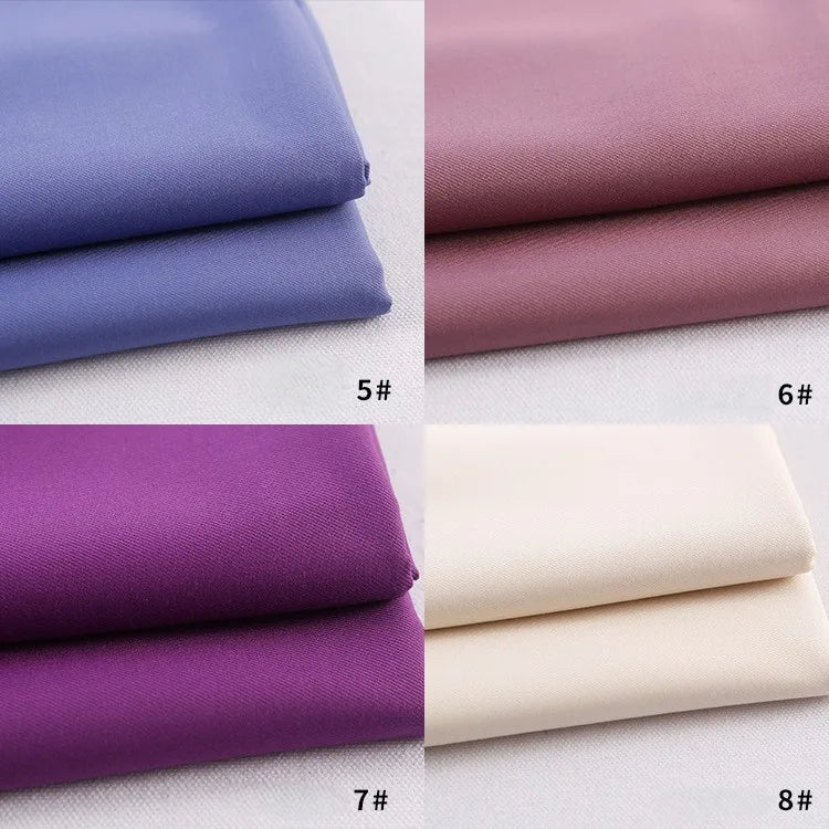 Quatre piles de gabardine Longan Craft France (#5 bleu, #6 mauve, #7 violet, #8 blanc cassé) sont soigneusement disposées en grille sur une surface claire - un textile polyester-rayon idéal pour les uniformes ou les projets de bricolage.