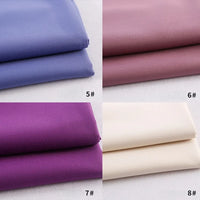 Quatre piles de gabardine Longan Craft France (#5 bleu, #6 mauve, #7 violet, #8 blanc cassé) sont soigneusement disposées en grille sur une surface claire - un textile polyester-rayon idéal pour les uniformes ou les projets de bricolage.