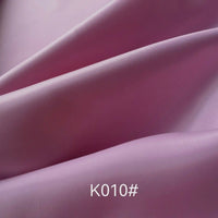 Gros plan sur un tissu satiné coloré en viscose au mètre (Longan Craft France) aux plis souples et légèrement brillants. Le texte "K010#" se trouve en bas au centre, mettant en valeur ce tissu idéal pour les robes de cérémonie.
